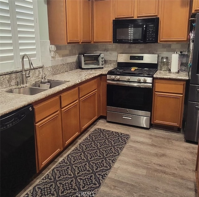 kitchen with light wood-type flooring, backsplash, sink, and black appliances