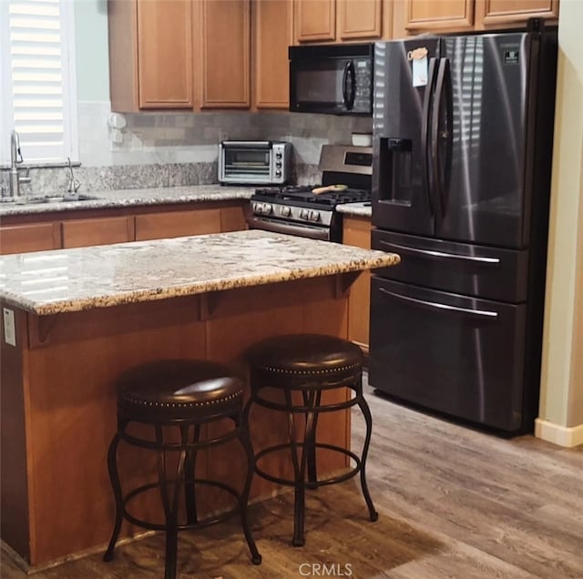 kitchen featuring sink, light wood-type flooring, decorative backsplash, light stone counters, and black appliances