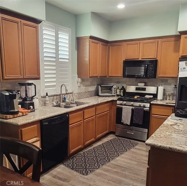 kitchen with light wood-type flooring, sink, decorative backsplash, and black appliances