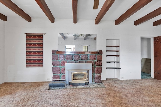 unfurnished living room featuring carpet, ceiling fan, beam ceiling, a wood stove, and a fireplace