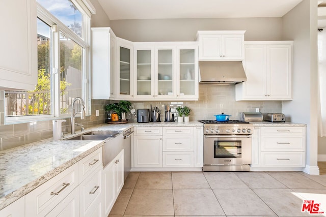 kitchen with tasteful backsplash, stainless steel stove, wall chimney exhaust hood, and light tile patterned floors