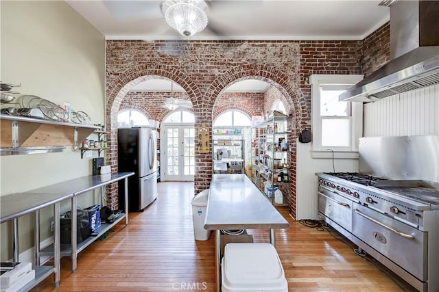 455 W 20th St, Merced, CA 95340 - kitchen featuring light hardwood / wood-style flooring, appliances with stainless steel finishes, brick wall, french doors, and wall chimney exhaust hood