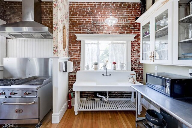455 W 20th St, Merced, CA 95340 - kitchen with wall chimney exhaust hood, white cabinetry, decorative light fixtures, light wood-type flooring, and brick wall