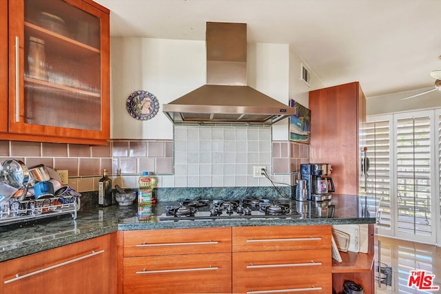 kitchen with backsplash, tile patterned floors, wall chimney exhaust hood, stainless steel gas cooktop, and dark stone countertops