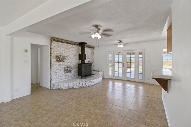 unfurnished living room featuring french doors, a textured ceiling, light tile patterned flooring, a wood stove, and ceiling fan