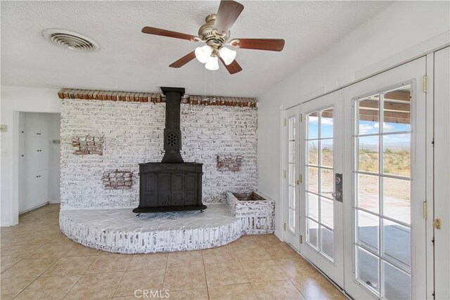 unfurnished living room featuring light tile patterned floors, french doors, a wood stove, and brick wall