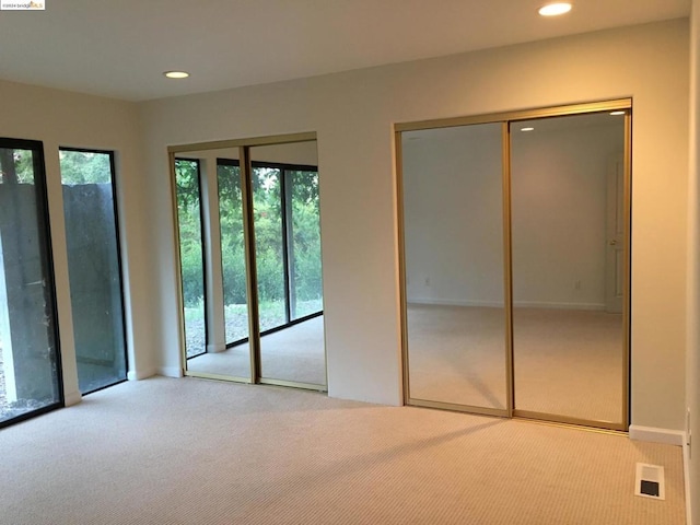 unfurnished bedroom with light colored carpet and multiple closets