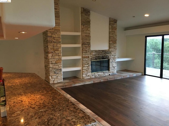 unfurnished living room with ornate columns, wood-type flooring, built in features, and a stone fireplace