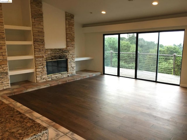 unfurnished living room featuring wood-type flooring, a stone fireplace, vaulted ceiling, and built in shelves