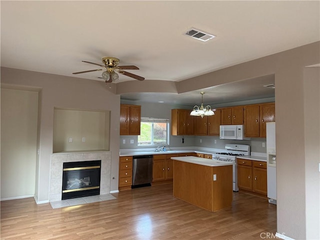 kitchen with pendant lighting, sink, white appliances, a center island, and light hardwood / wood-style floors