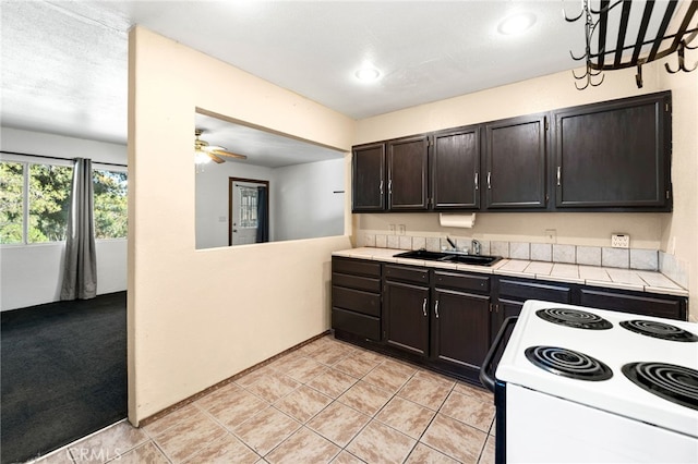 kitchen featuring ceiling fan with notable chandelier, light carpet, sink, dark brown cabinetry, and range