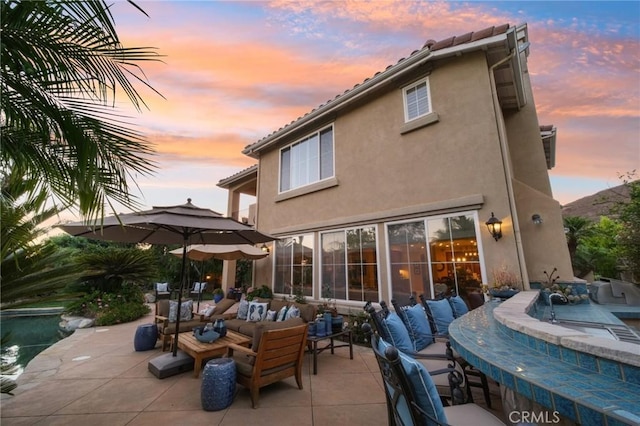 back house at dusk featuring exterior bar, an outdoor hangout area, and a patio