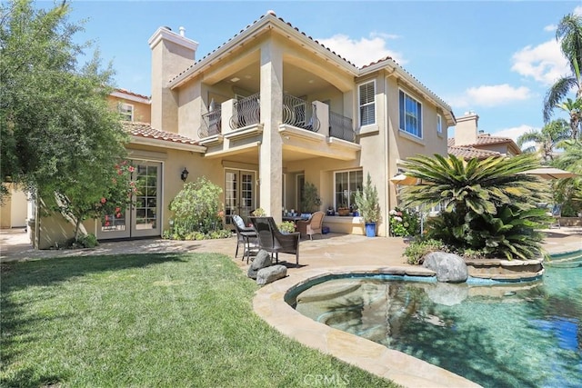 rear view of property with french doors, a balcony, a patio area, and a lawn