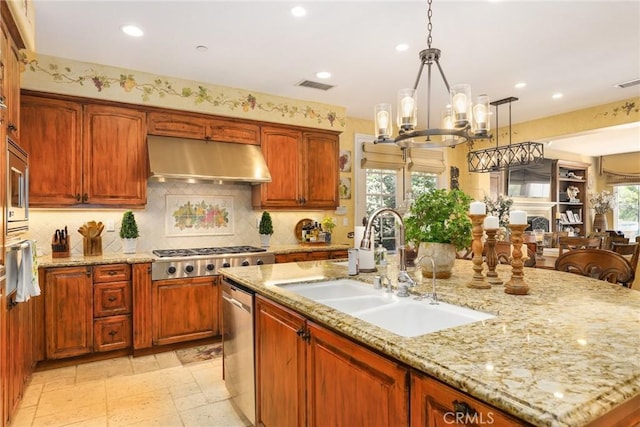 kitchen with extractor fan, appliances with stainless steel finishes, sink, hanging light fixtures, and a kitchen island with sink