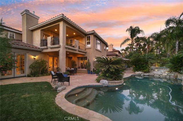 back house at dusk featuring a patio, french doors, and a balcony