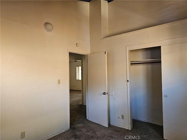 unfurnished bedroom with dark carpet, a high ceiling, and a closet