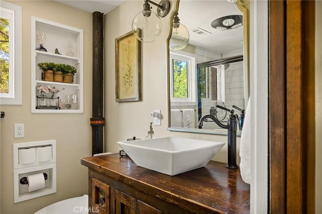 bathroom with built in shelves, vanity, an enclosed shower, and toilet