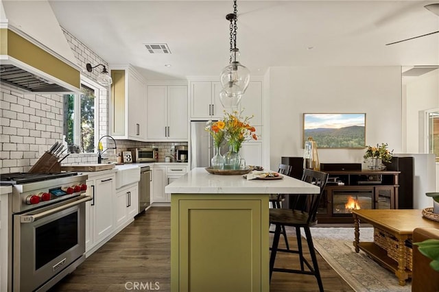 kitchen featuring appliances with stainless steel finishes, custom exhaust hood, a kitchen island, white cabinetry, and a breakfast bar area