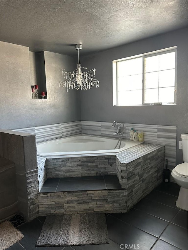 bathroom featuring an inviting chandelier, toilet, tiled bath, and a textured ceiling