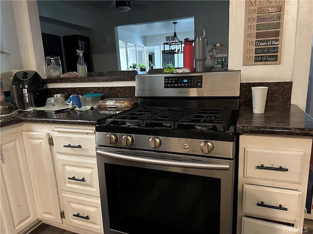 kitchen with kitchen peninsula, stainless steel gas range oven, dark stone counters, and a chandelier