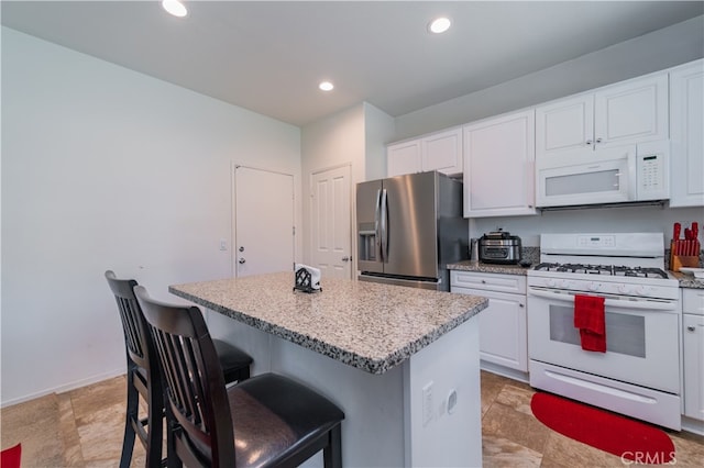 kitchen with light tile patterned floors, white cabinets, white appliances, and a center island