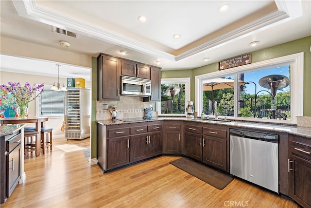 kitchen with light wood-type flooring, a raised ceiling, stainless steel appliances, and decorative light fixtures