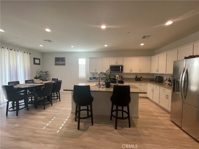 kitchen featuring appliances with stainless steel finishes, light stone counters, white cabinets, a kitchen breakfast bar, and a center island