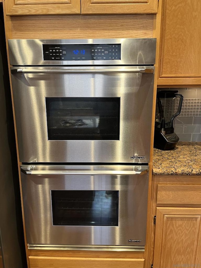 details featuring light stone counters, double oven, and tasteful backsplash