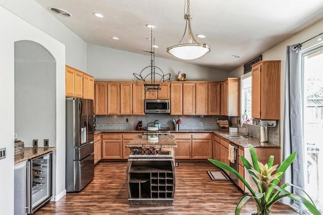 kitchen with pendant lighting, beverage cooler, appliances with stainless steel finishes, lofted ceiling, and dark stone countertops