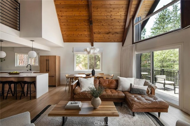 living room featuring plenty of natural light, light wood-type flooring, high vaulted ceiling, and an inviting chandelier