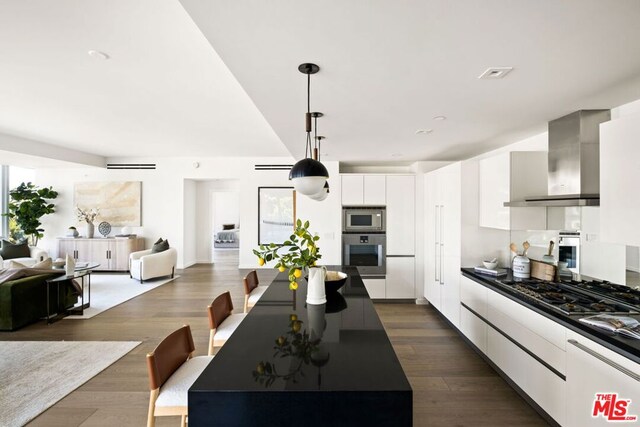 kitchen featuring dark hardwood / wood-style flooring, white cabinetry, gas stovetop, wall chimney exhaust hood, and decorative light fixtures