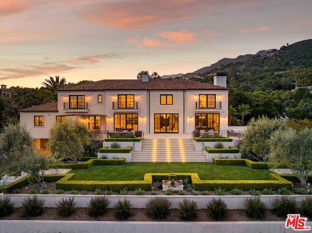 back house at dusk with a lawn and a mountain view