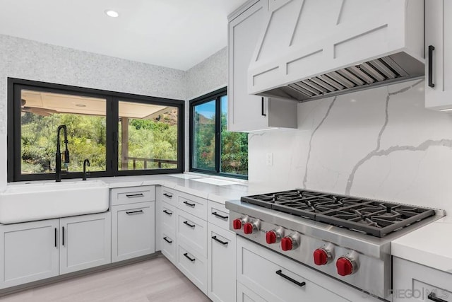 kitchen with tasteful backsplash, premium range hood, sink, stainless steel gas cooktop, and white cabinets