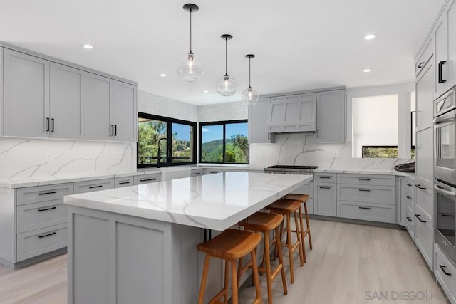 kitchen with a breakfast bar area, gray cabinetry, light wood-type flooring, light stone countertops, and a center island