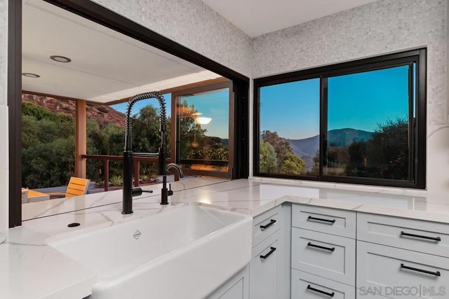 interior space with white cabinets, light stone counters, sink, and a mountain view