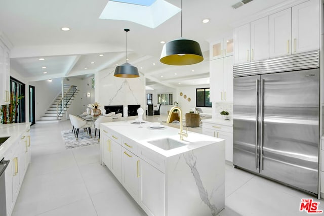 kitchen featuring white cabinets, a skylight, an island with sink, and stainless steel appliances