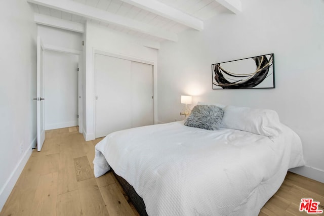 bedroom with beam ceiling, a closet, and wood-type flooring