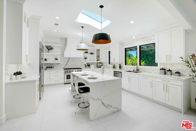 kitchen with a skylight, premium range hood, an island with sink, decorative backsplash, and white cabinets