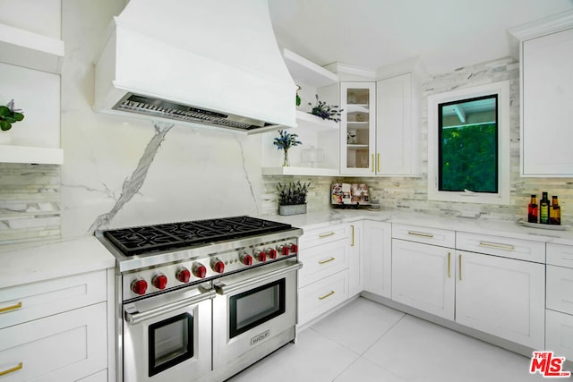 kitchen with white cabinets, tasteful backsplash, range with two ovens, and exhaust hood