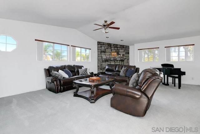 carpeted living room with ceiling fan, a stone fireplace, and vaulted ceiling