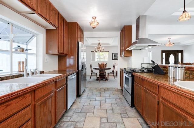 kitchen featuring appliances with stainless steel finishes, hanging light fixtures, wall chimney exhaust hood, an inviting chandelier, and sink