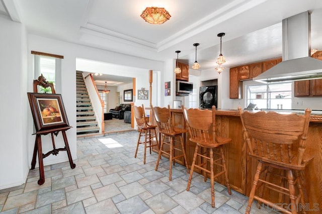 kitchen with a breakfast bar, a tray ceiling, island exhaust hood, and plenty of natural light