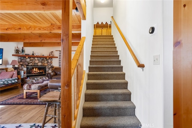 stairs featuring hardwood / wood-style floors, wooden ceiling, beamed ceiling, and a fireplace