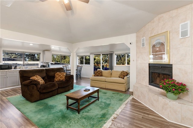 living room featuring ceiling fan, a tiled fireplace, hardwood / wood-style floors, and vaulted ceiling