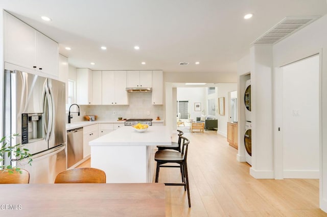 kitchen featuring light hardwood / wood-style flooring, white cabinetry, stainless steel appliances, a breakfast bar area, and stacked washer / drying machine