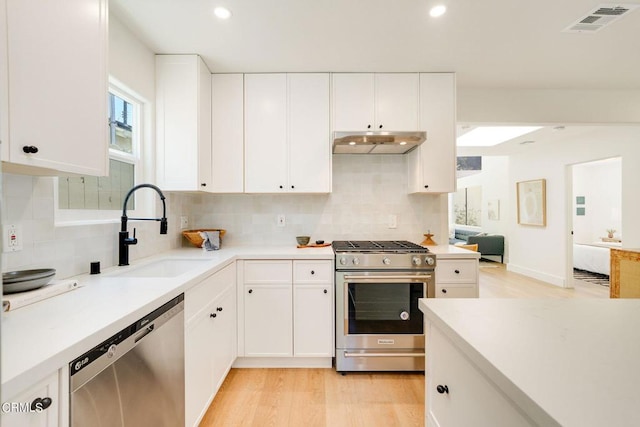 kitchen with appliances with stainless steel finishes, light wood-type flooring, white cabinetry, and sink