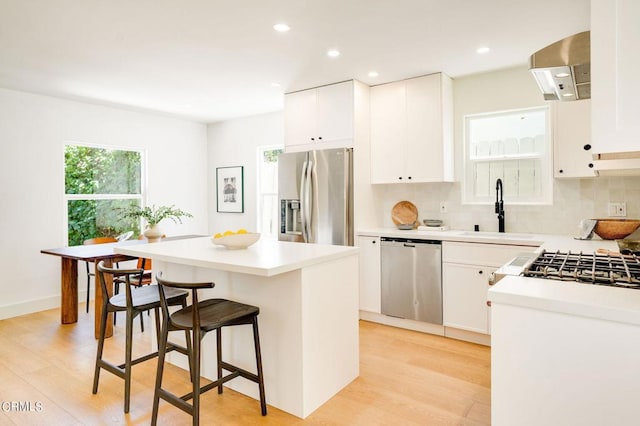 kitchen featuring a kitchen island, light wood-type flooring, stainless steel appliances, sink, and white cabinetry