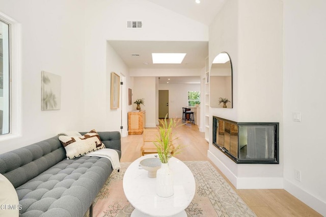 living room with light hardwood / wood-style floors, a multi sided fireplace, high vaulted ceiling, and a skylight