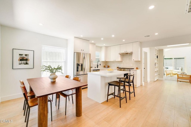 kitchen featuring light hardwood / wood-style flooring, backsplash, white cabinetry, appliances with stainless steel finishes, and a center island