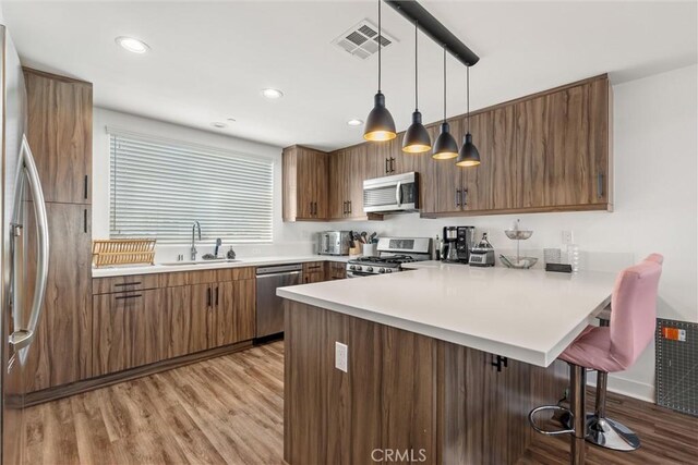 kitchen featuring light hardwood / wood-style flooring, hanging light fixtures, a kitchen bar, appliances with stainless steel finishes, and kitchen peninsula